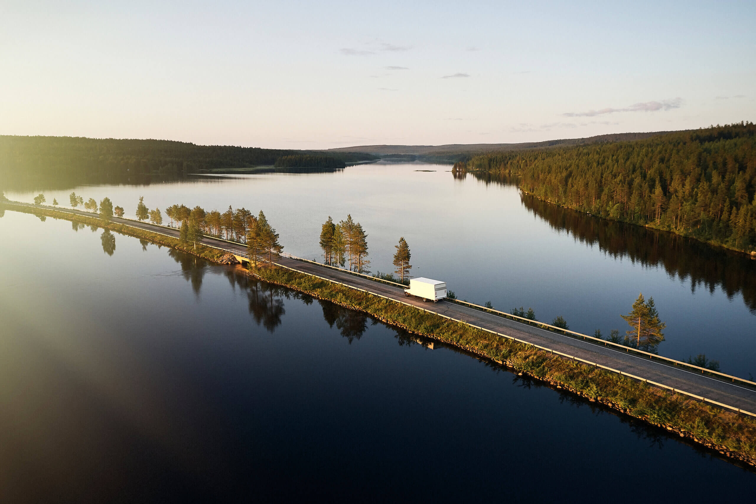 Autoja ajamassa järvimaisemaa halkovalla tiellä.